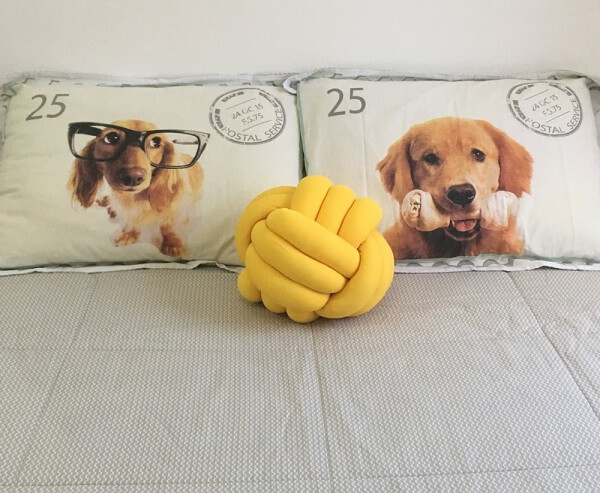 The yellow knotted pillow on the bed brings joy to the environment